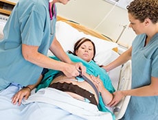 Female nurses preparing pregnant woman for fetal heart rate monitor in hospital room