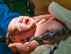 New born baby boy with umbilical cord assisted by midwife